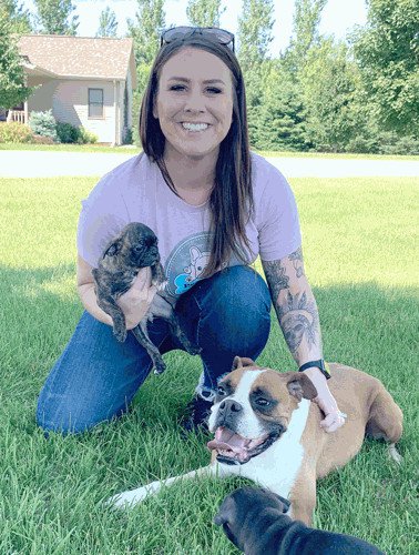 A woman sitting with three dogs and smiling at the camera.